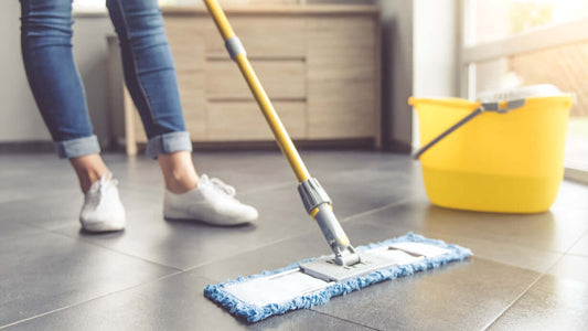 Person mopping a tiled floor with a mop and yellow bucket, illustrating effective cleaning services.
