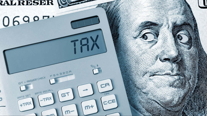 Calculator displaying 'TAX' next to a hundred dollar bill illustrating tax deductions.