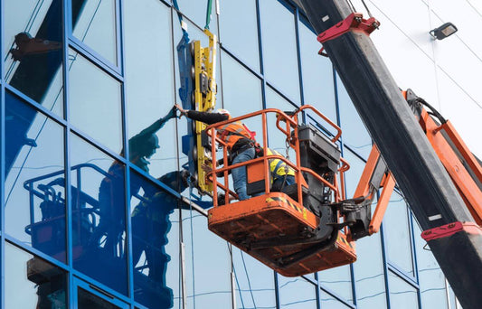 Professional window cleaners using an elevated lift to clean large glass windows in Copenhagen.